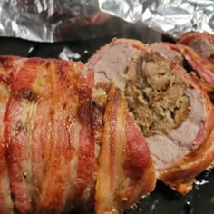 bacon wrapped in tin foil sitting on top of a pan filled with meat and vegetables