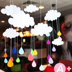 some paper clouds hanging from the ceiling with rain drops on them, and one cloud is colored