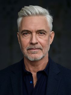 an older man with white hair wearing a black suit and blue shirt is looking at the camera