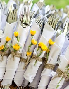 yellow flowers are tied to napkins with silverware in the backgroung