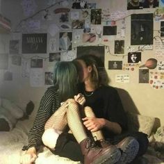 two people sitting on a bed kissing each other with pictures all over the wall behind them