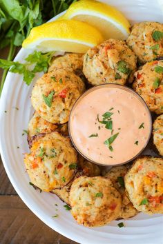 a white plate topped with crab cakes next to a lemon wedge and garnish