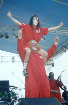 two people dressed as clowns on stage at an outdoor music festival, one holding the other up in the air