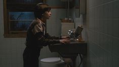 a young boy standing in front of a bathroom sink with his hands on the faucet