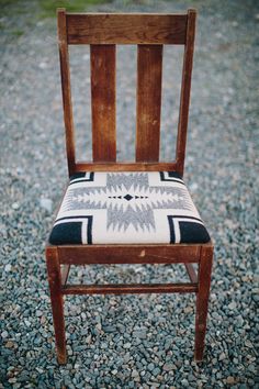 a wooden chair with a black and white seat pad sitting on top of gravel covered ground