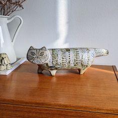 a cat figurine sitting on top of a wooden table next to a vase