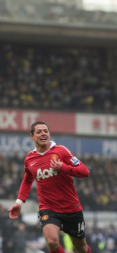 a man in red shirt kicking a soccer ball on field with people watching from the stands