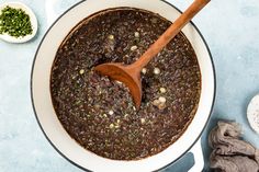 a wooden spoon in a pot filled with black beans and other ingredients on a blue surface