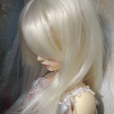 a doll with long white hair sitting on top of a bed next to a curtain