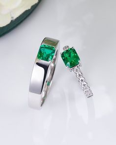 two rings with green and white stones on them sitting next to each other in front of a flower