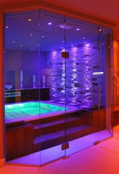 an indoor swimming pool with purple lighting and stone walls in the background, surrounded by glass doors