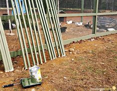 a can of paint sitting on the ground next to a fence with chickens behind it