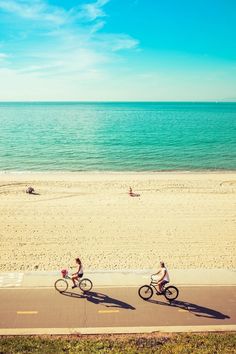 two people riding bikes on the beach near the ocean