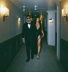 a man in a tuxedo walking down a hallway next to a woman in a black dress