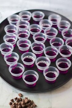 several cups filled with purple liquid sitting on top of a black plate next to chocolate chips