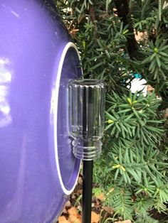 a close up of a purple bird feeder in front of some trees and bushes with leaves