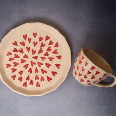 a white and red plate with hearts painted on it next to a cup that has a saucer