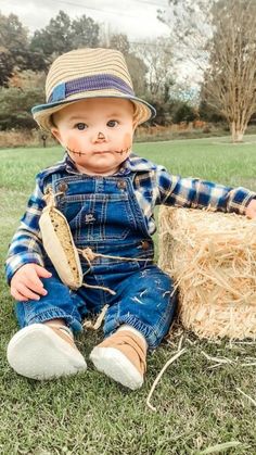 a baby sitting in the grass wearing overalls and a straw hat with his mouth open