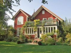 a red house with white windows and balconies on the second story is surrounded by greenery