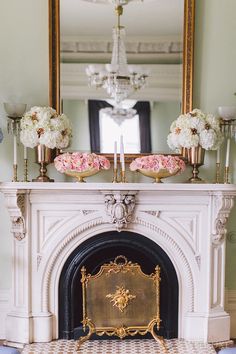 the fireplace is decorated with pink flowers and gold candlesticks, along with white hydrangeas