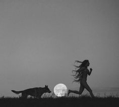 a woman running in the grass with a cat next to her and a full moon behind her