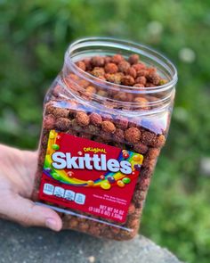 a hand holding a jar filled with skittles on top of a stone wall