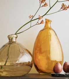 two vases sitting on top of a table with fruit and flowers in them next to each other