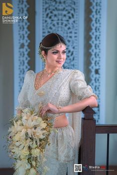 a woman in a white sari holding a bridal bouquet and posing for the camera