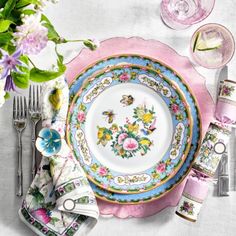 a table setting with pink and blue plates, silverware, flowers and napkins