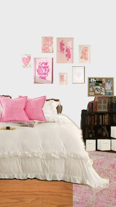 a white bed with pink pillows and pictures on the wall