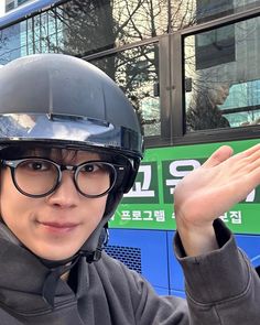 a man wearing a helmet and glasses waves to the camera while standing in front of a double decker bus