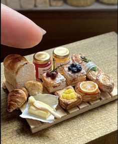 a miniature tray with bread, jams and other pastries on it is being held by a finger