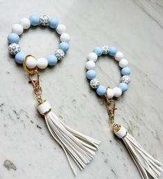 two white and blue beads with tassels are on a marble countertop next to each other