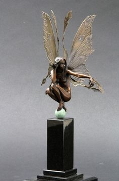 a bronze statue of a fairy with wings on top of a black base, holding a green ball