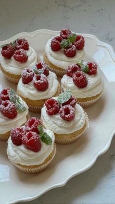 small cupcakes with white frosting and raspberries on top sit on a plate