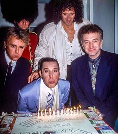 the three men are sitting in front of a cake with candles on it