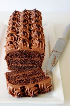 a cake with chocolate frosting sitting on top of a white plate next to a knife