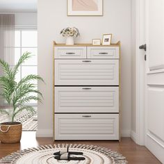 a white dresser sitting in a living room next to a potted plant on top of a rug