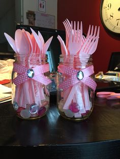 two mason jars with pink utensils in them on a table next to a clock