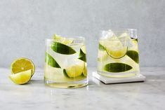 two glasses filled with lemonade and lime slices on top of a marble countertop