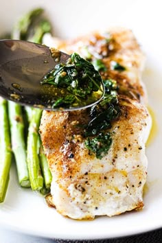 a white plate topped with fish covered in sauce and broccoli next to a fork