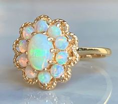 "Opal ring, vintage Australian opal engagement ring in 14k yellow gold. Beautiful center opal stone with wonderful blue and green color hues. Center stone measures 7mm x 5mm (about .55 carat). Ten accompanying stones measure ~2.8mm each and are superbly matched with the main opal, estimated .08 carat each. Total opal carat weight for the ring is estimated 1.19 carats. Excellent condition! Ring weighs 3.4 grams. Size 6 and can be sized +- 3.5 sizes by adding sizing to your order for 45- here: htt Yellow Gold Ethiopian Opal Anniversary Ring, Yellow Gold Ethiopian Opal Ring For Anniversary, Anniversary Ethiopian Opal Ring In Yellow Gold, Heirloom Ethiopian Opal Ring For Wedding, Heirloom Ethiopian Opal Wedding Ring, Opal Cabochon Ring In 14k Gold For Anniversary, 14k Gold Cabochon Opal Anniversary Ring, 14k Gold Cabochon Opal Ring For Anniversary, Heirloom Style Round Opal Ring