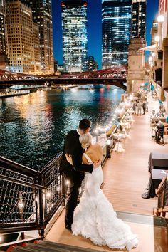 a bride and groom kissing on the balcony of a restaurant overlooking the river in new york city