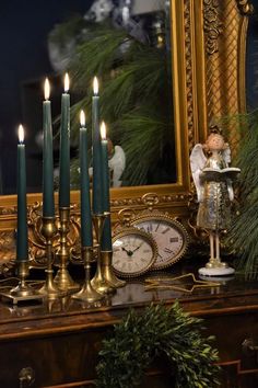 a table topped with candles and a clock next to a mirror covered in greenery