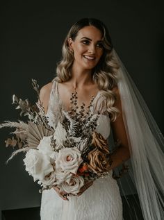 a woman wearing a wedding dress holding a bouquet of flowers and feathers in her hands