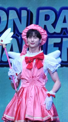 a woman in a pink dress and red bow tie holding a white umbrella on stage