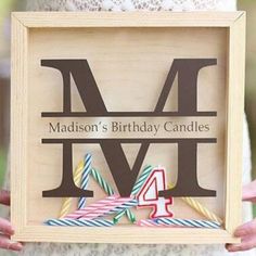 a woman holding up a wooden sign with candles in it's frame that says madison's birthday candles