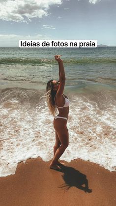 a woman standing on top of a sandy beach next to the ocean with her arms in the air