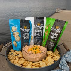 some chips and dip are sitting in a bowl on the ground next to a body of water