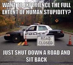 a police car parked in front of a road closed sign that says, want to experience the full extent of human stupidity? just shut down a road and sit back